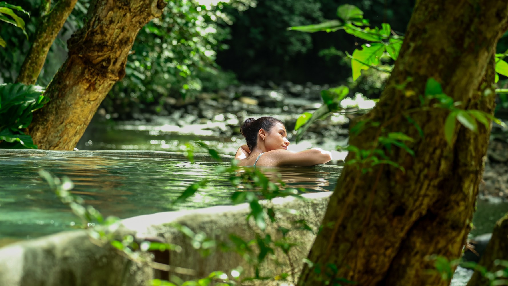 Mujer relajándose en una piscina natural rodeada de árboles y vegetación.