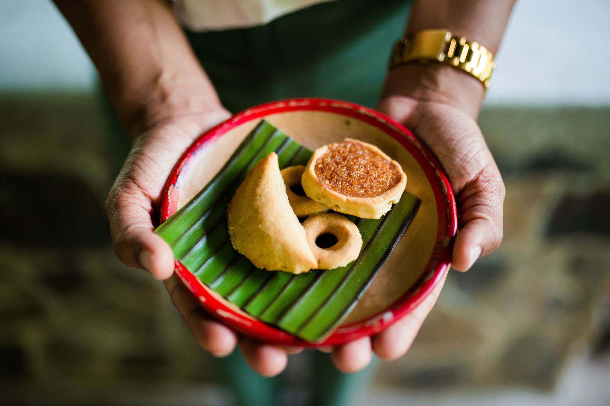 Hands holding a plate with assorted pastries on a banana leaf.