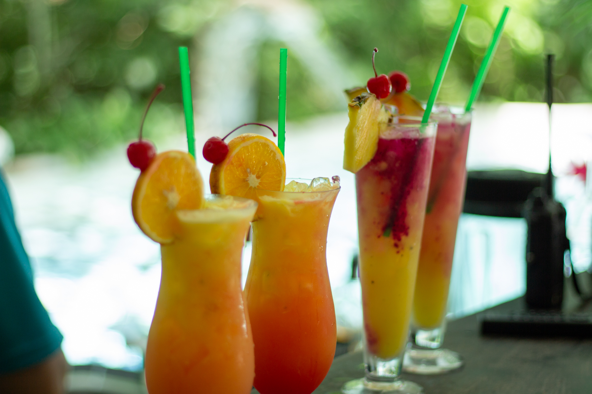 Colorful tropical drinks with straws, garnished with orange slices and cherries on a bar counter.
