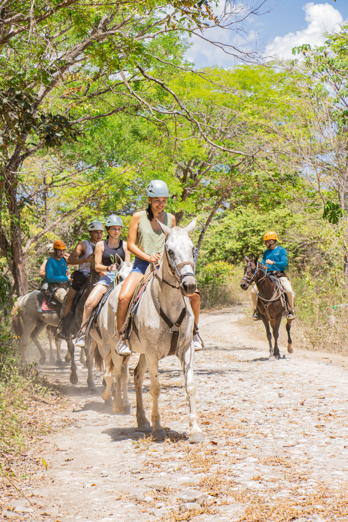 Group of people riding horses on a dirt path through lush greenery.